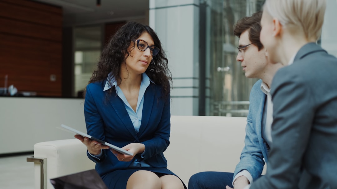 Businesswoman in glasses talking and duscussing future contract with business partners sitting on couch in modern office indoors